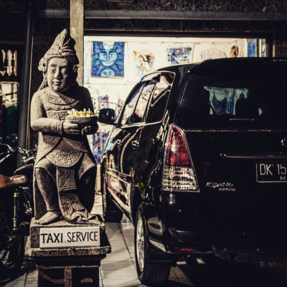 Balinese statue with a taxi service sign